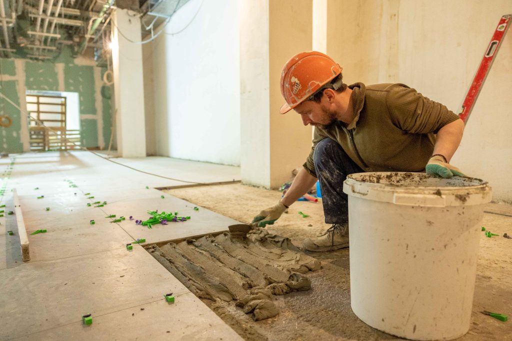 A professional contractor applying mortar to the back of a large natural stone tile during floor installation