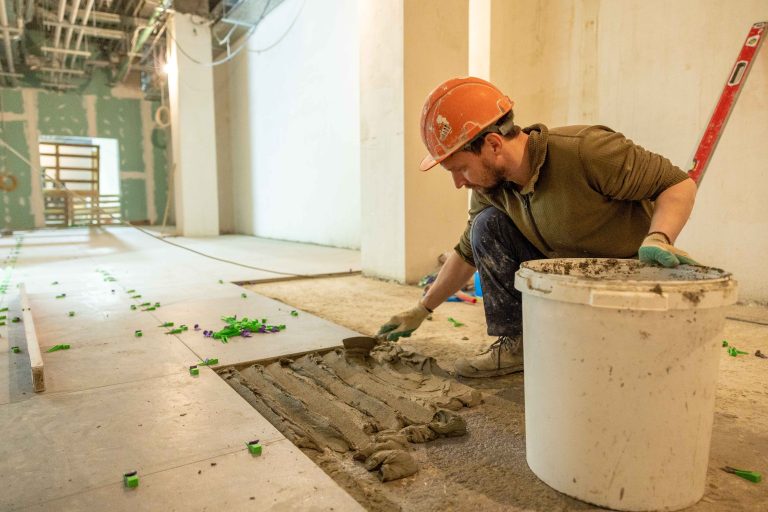 A professional contractor applying mortar to the back of a large natural stone tile during floor installation